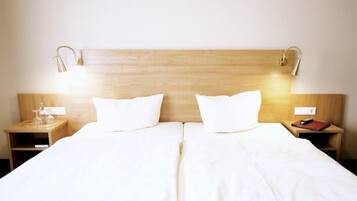 Un lit double avec du linge de lit blanc, deux tables de chevet avec des lampes et une tête de lit en bois.