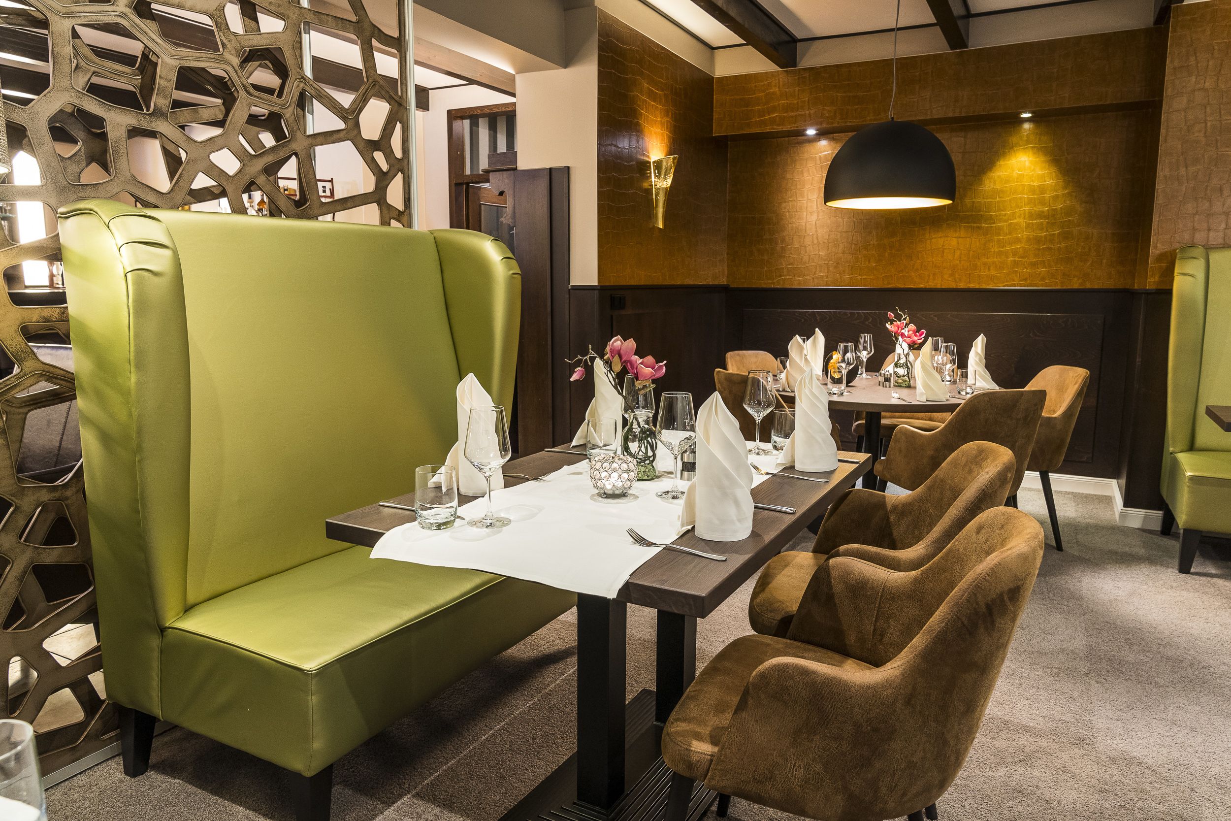 Restaurante com uma mesa comprida posta para refeição, cadeiras estofadas verdes e design de interiores moderno.