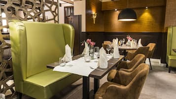 Restaurante com uma mesa comprida posta para refeição, cadeiras estofadas verdes e design de interiores moderno.