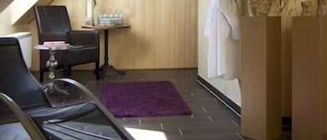 A modern spa room with a sloped ceiling, a massage table, a small table with a vase, and a wall-mounted clock.