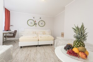 A modern hotel room with a white bed, a desk with a chair, a bicycle mounted on the wall, and a fruit bowl on the side table. - Hotel Tiek (Meppen)