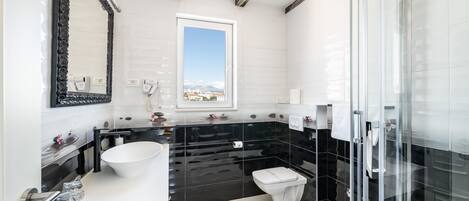 A modern bathroom with a large mirror, a white sink, a black vanity, a toilet, and a glass shower enclosure.
