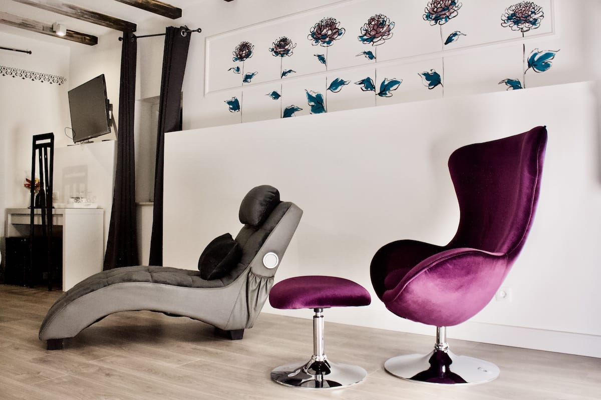 A modern room with a massage chair, a purple cushioned chair, and a wall with floral artwork.