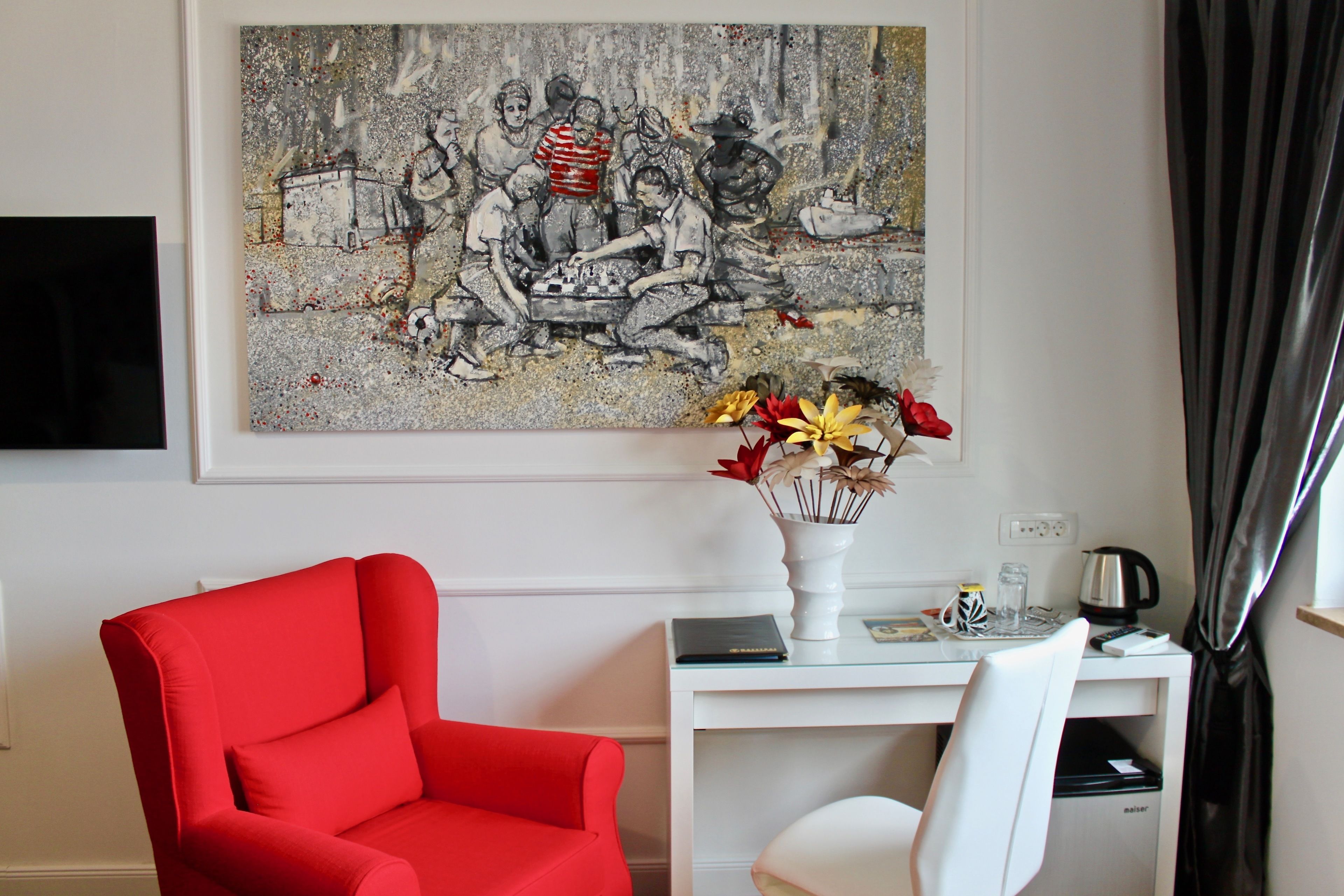 Una habitación con una silla roja, un escritorio blanco, un florero con flores y un cuadro en la pared.