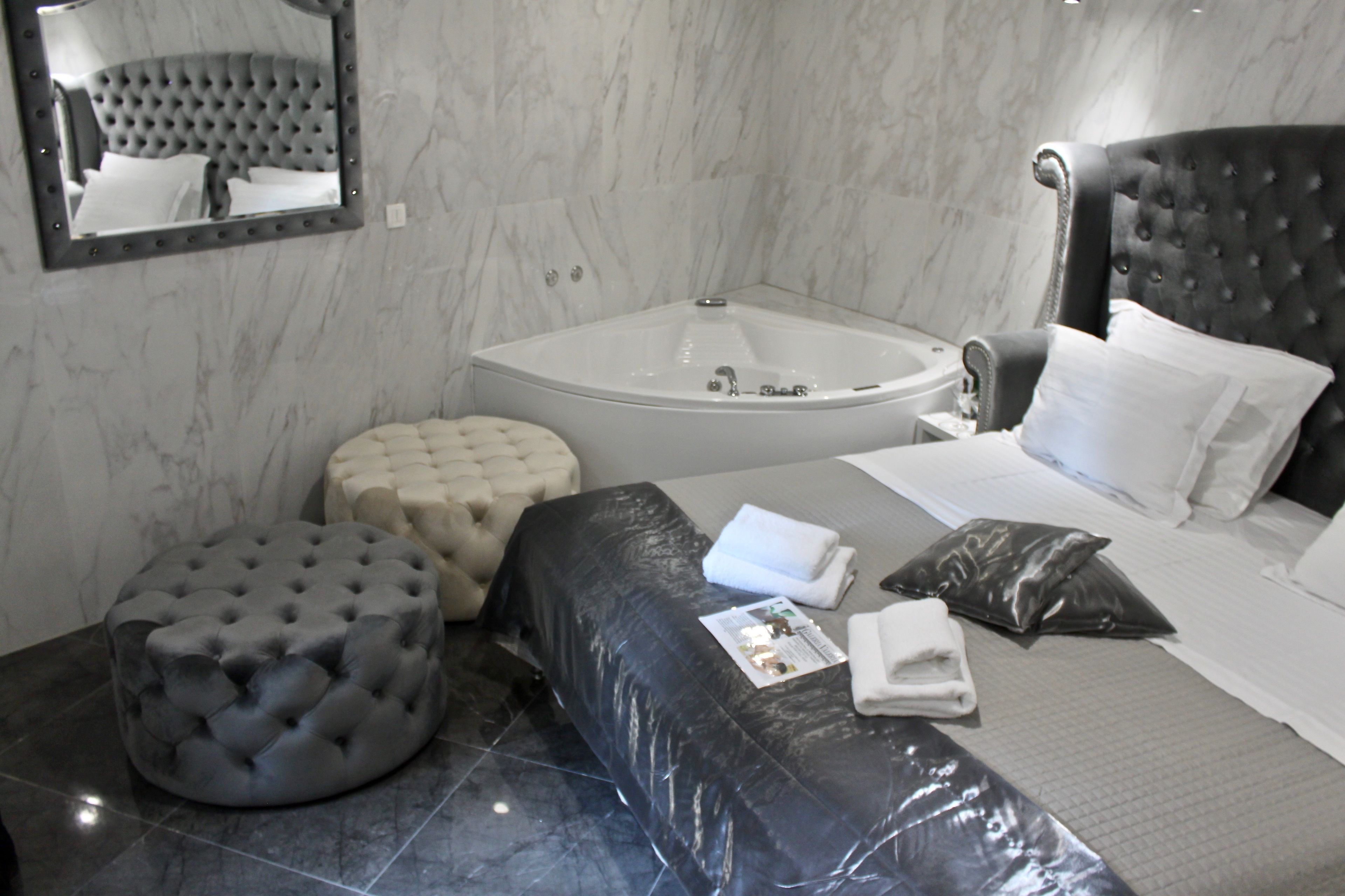 Una habitación de hotel moderna con una cama grande, un pouf redondo, un área de estar separada, una bañera y un espejo en la pared.