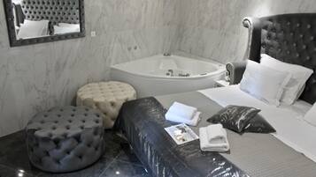 Una habitación de hotel moderna con una cama grande, un pouf redondo, un área de estar separada, una bañera y un espejo en la pared.