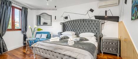 A bedroom with a large bed, a bedside table, a dresser, a mirror, and a chandelier.