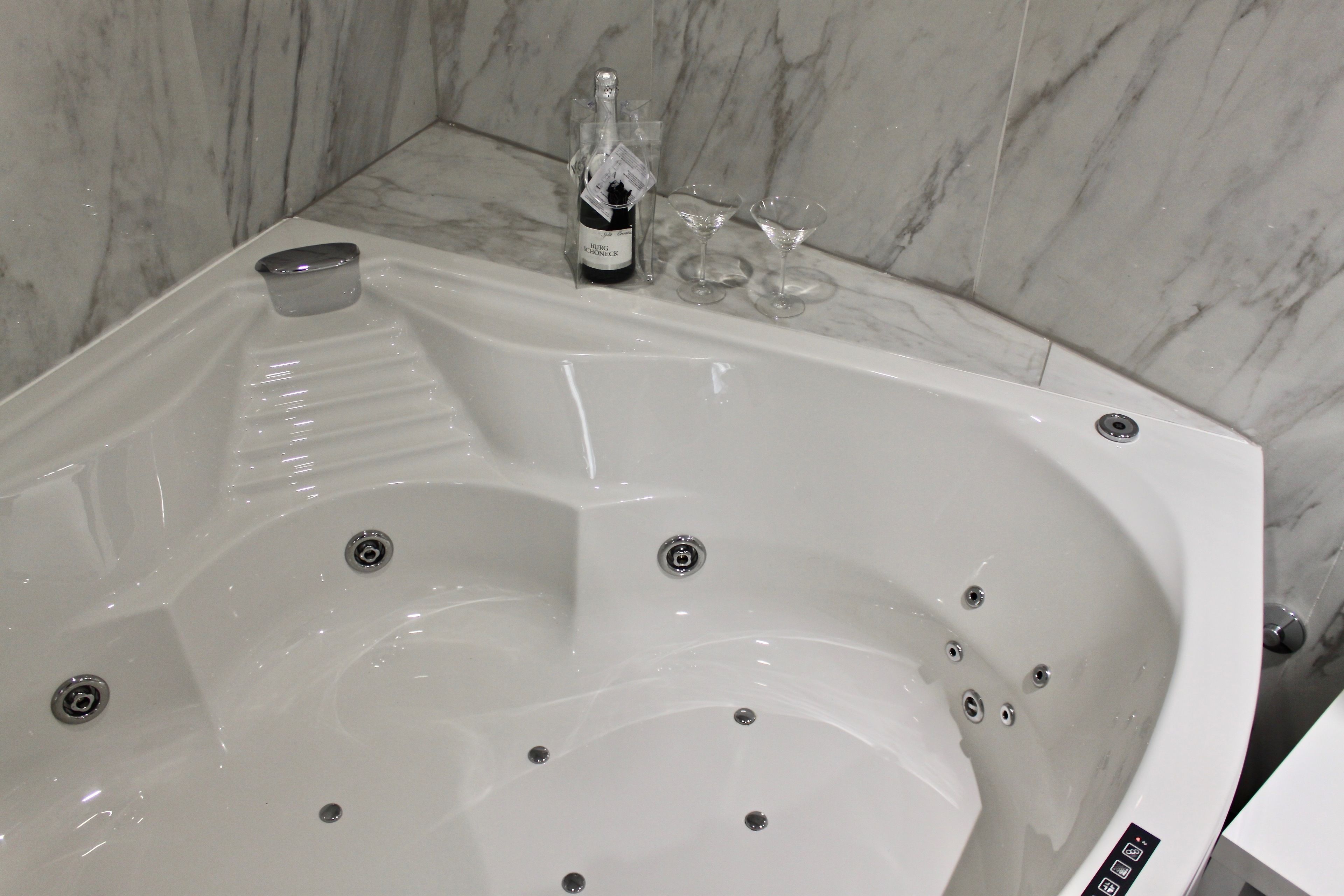 A modern bathroom with a marble wall, a large bathtub, and a bottle of champagne.