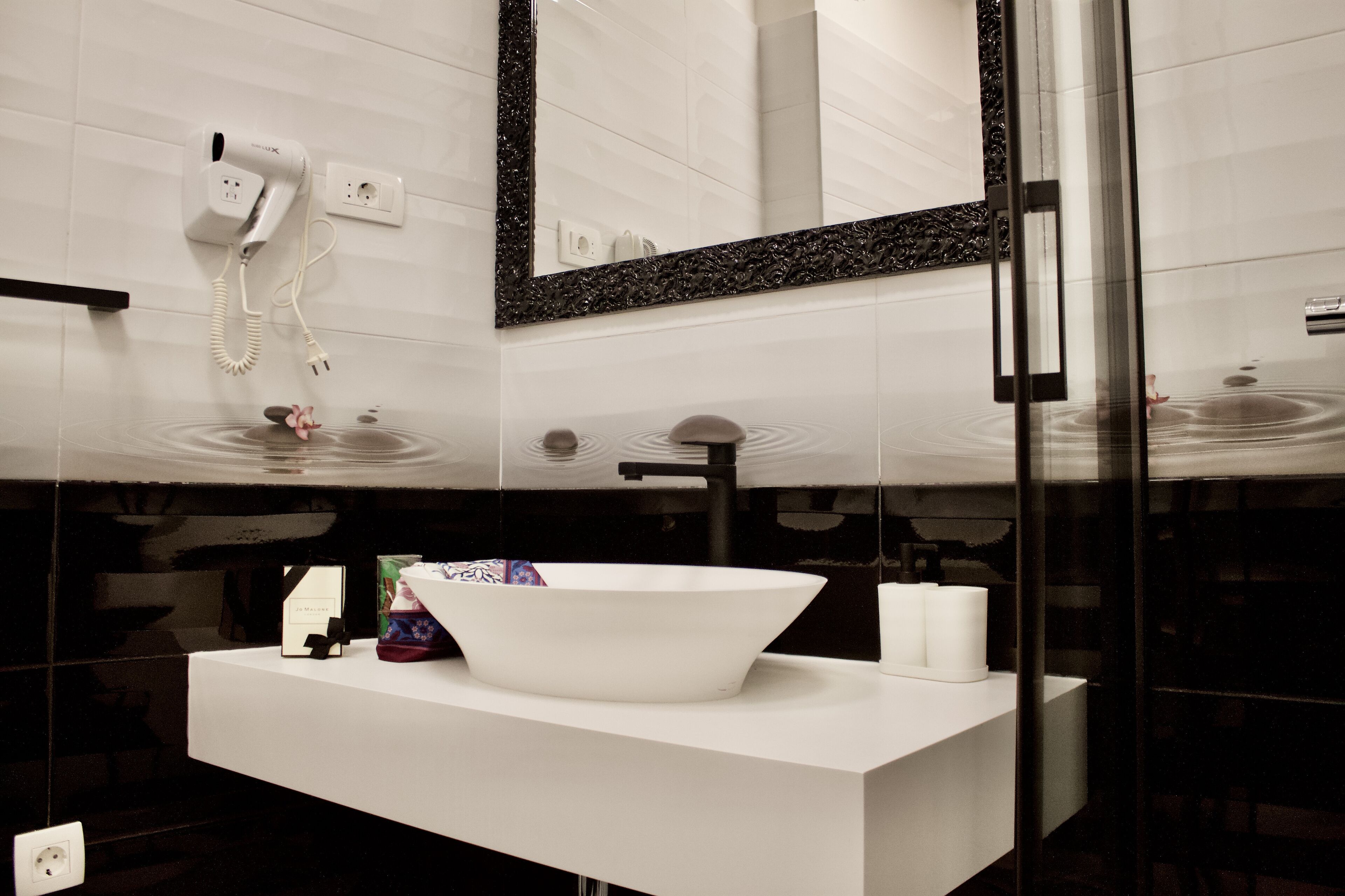 A modern bathroom with a white sink, a large mirror, and a hairdryer mounted on the wall.