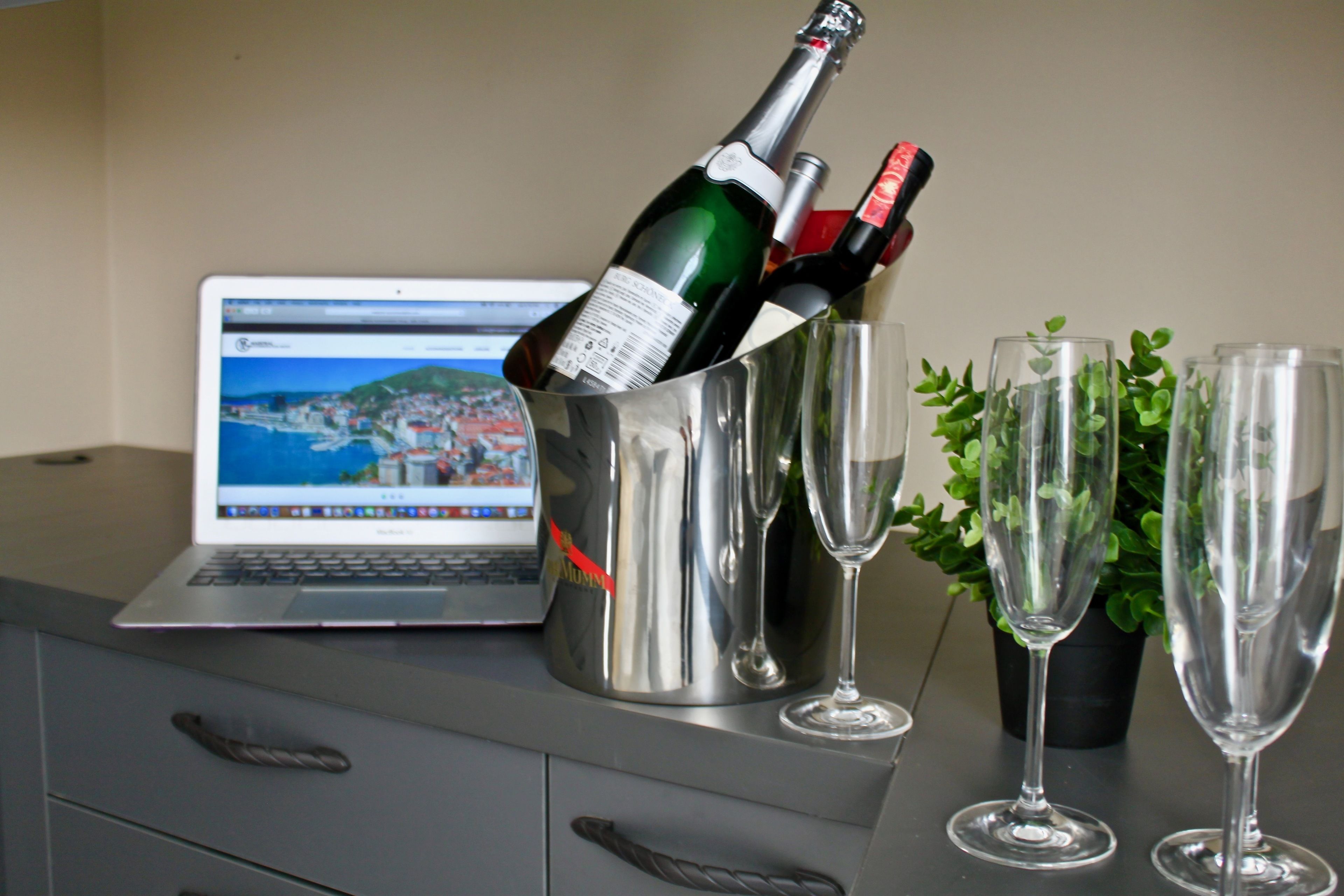 A laptop on a desk with a champagne bottle and glasses.