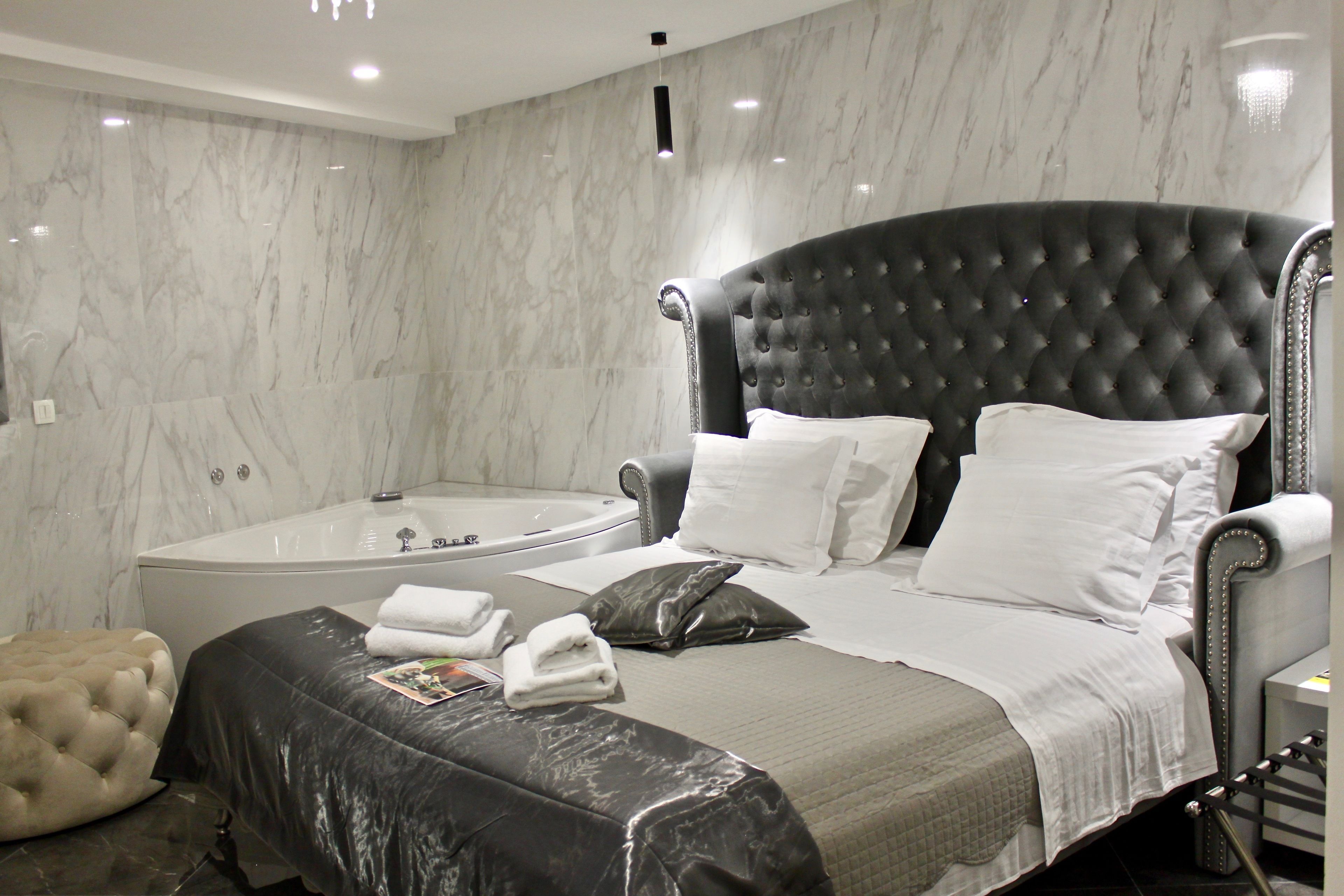 A modern bedroom with a large bed, a separate sitting area, a bathtub, and marble walls.