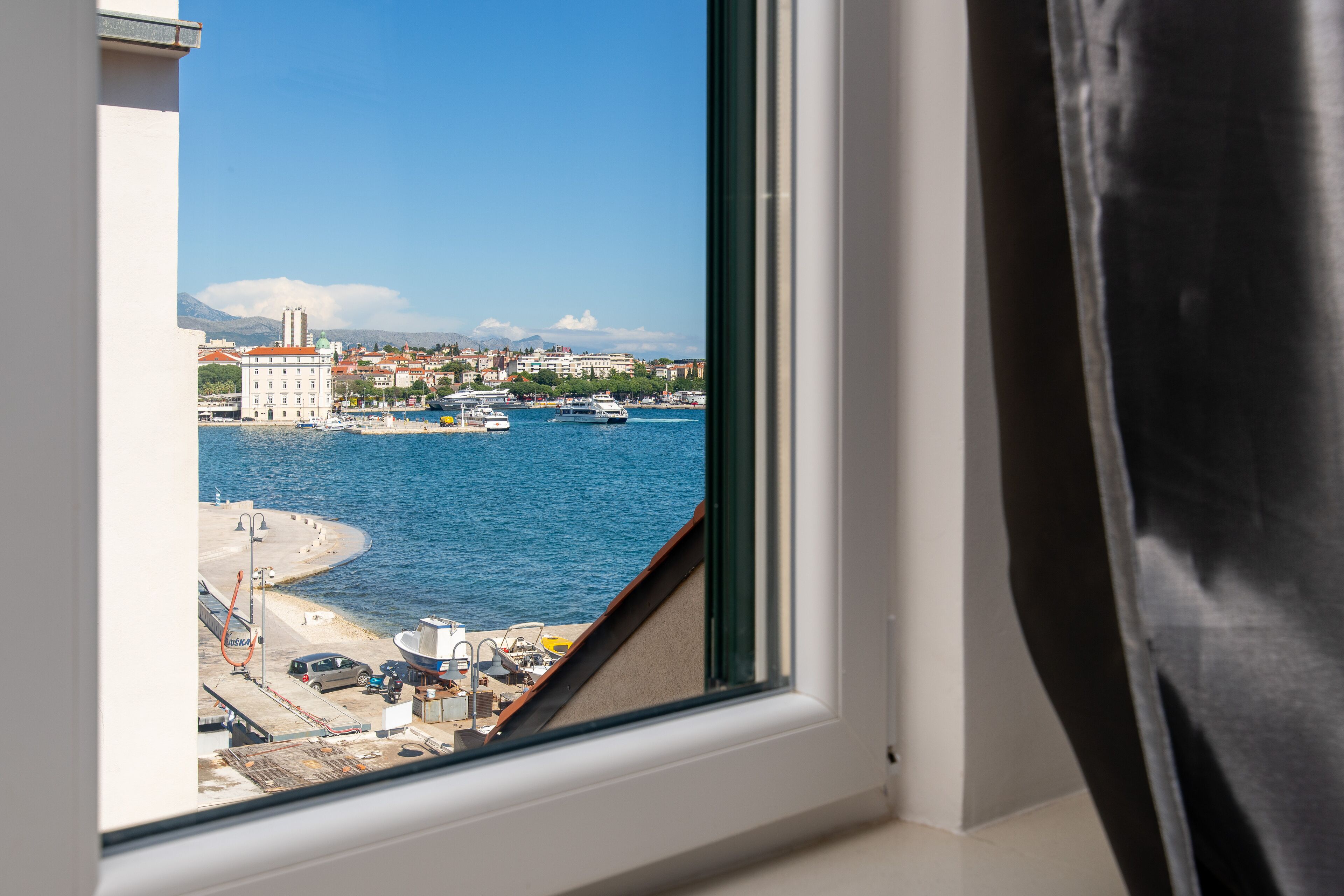 A window view of a coastal town with buildings, boats, and a clear blue sky.