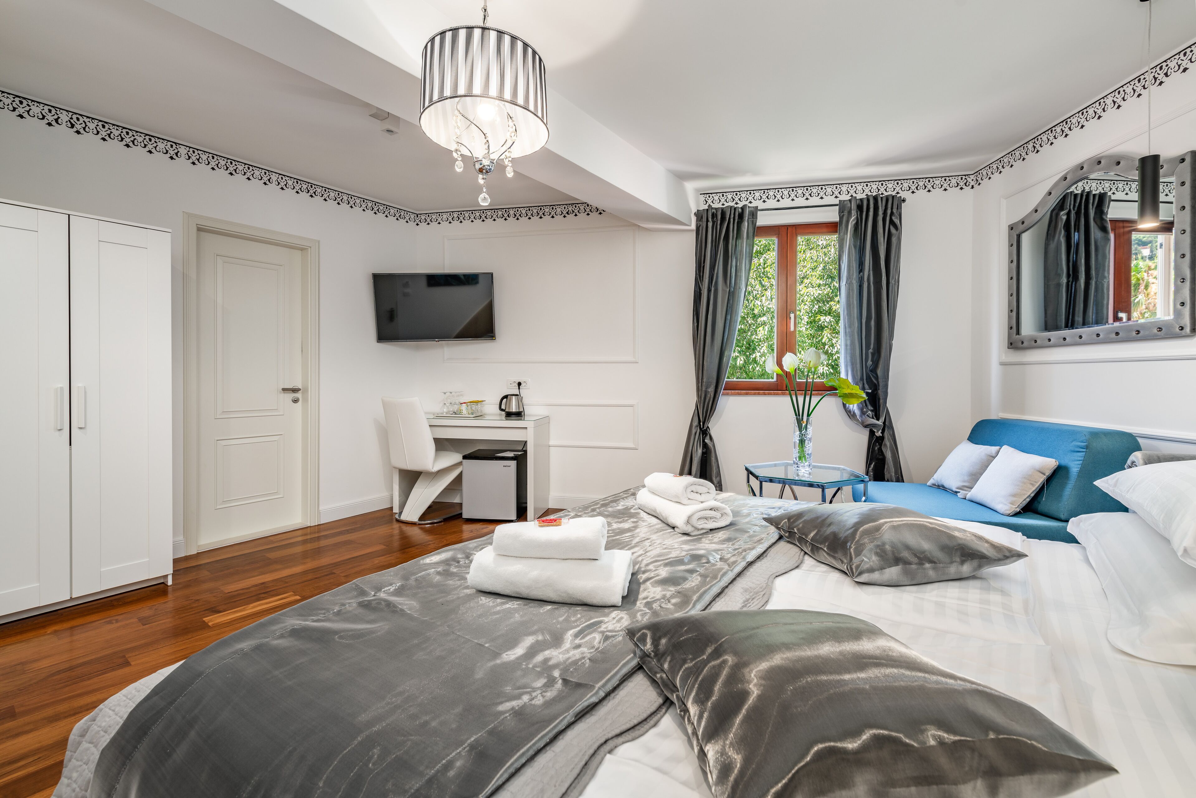 Un dormitorio con cama, escritorio, silla, televisión y ventana con cortinas.