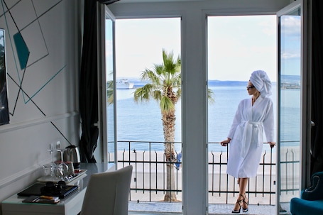 A room with a balcony, a palm tree, and a view of the sea.