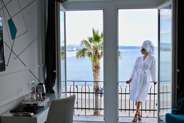 A room with a balcony, a palm tree, and a view of the sea.