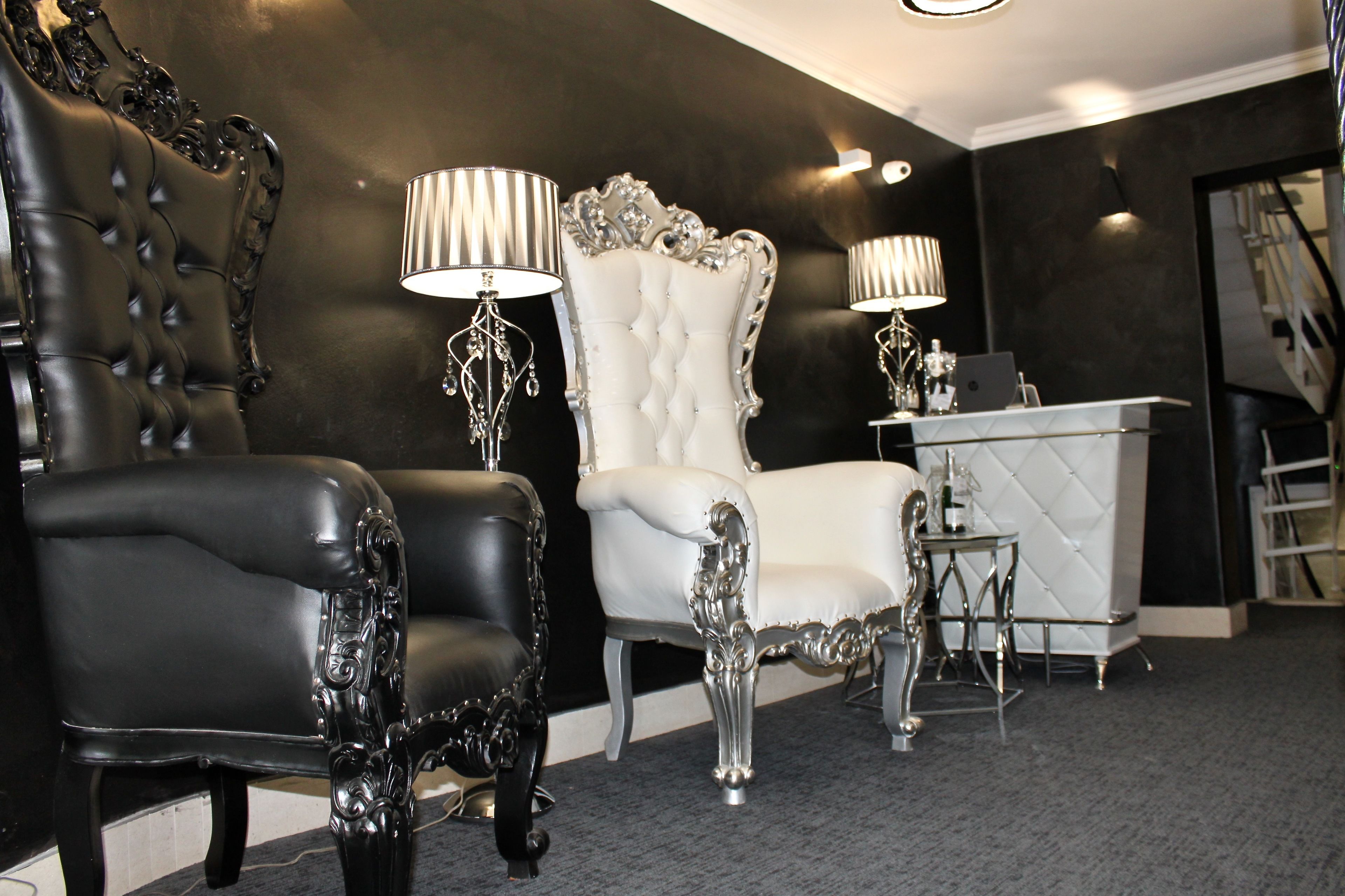A luxurious room with a black leather armchair, a white tufted chair, and a small table with a laptop.