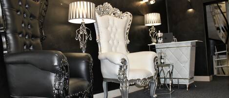 A luxurious room with a black leather armchair, a white tufted chair, and a small table with a laptop.