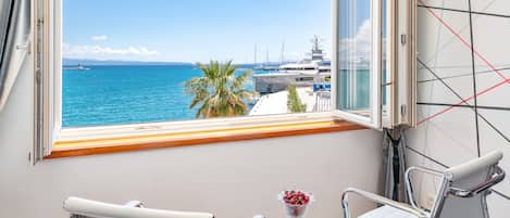 Una habitación con un gran ventanal con vistas a un puerto deportivo, una mesa con un jarrón de flores y dos sillas.