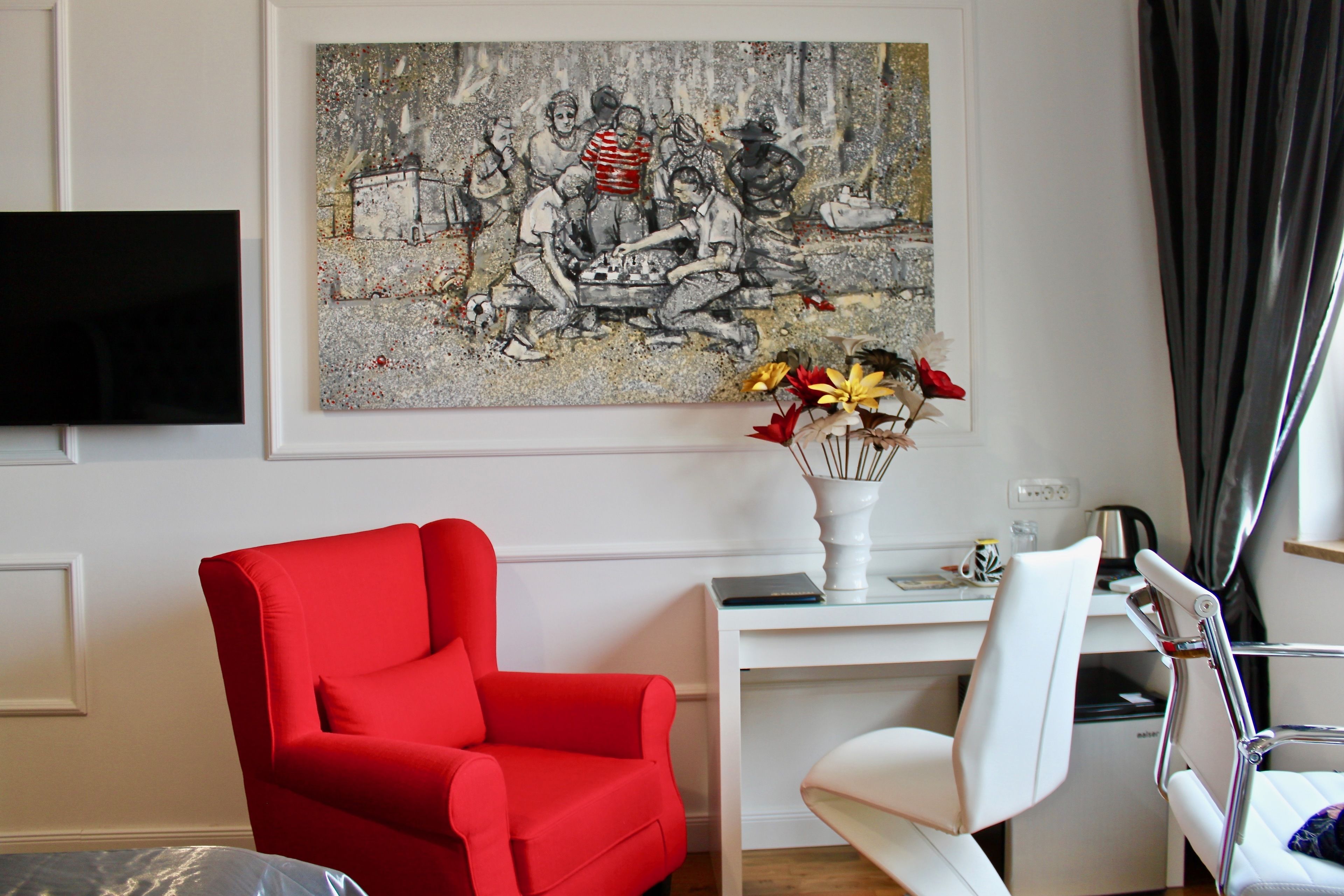 A room with a red armchair, a white desk, and a painting on the wall.