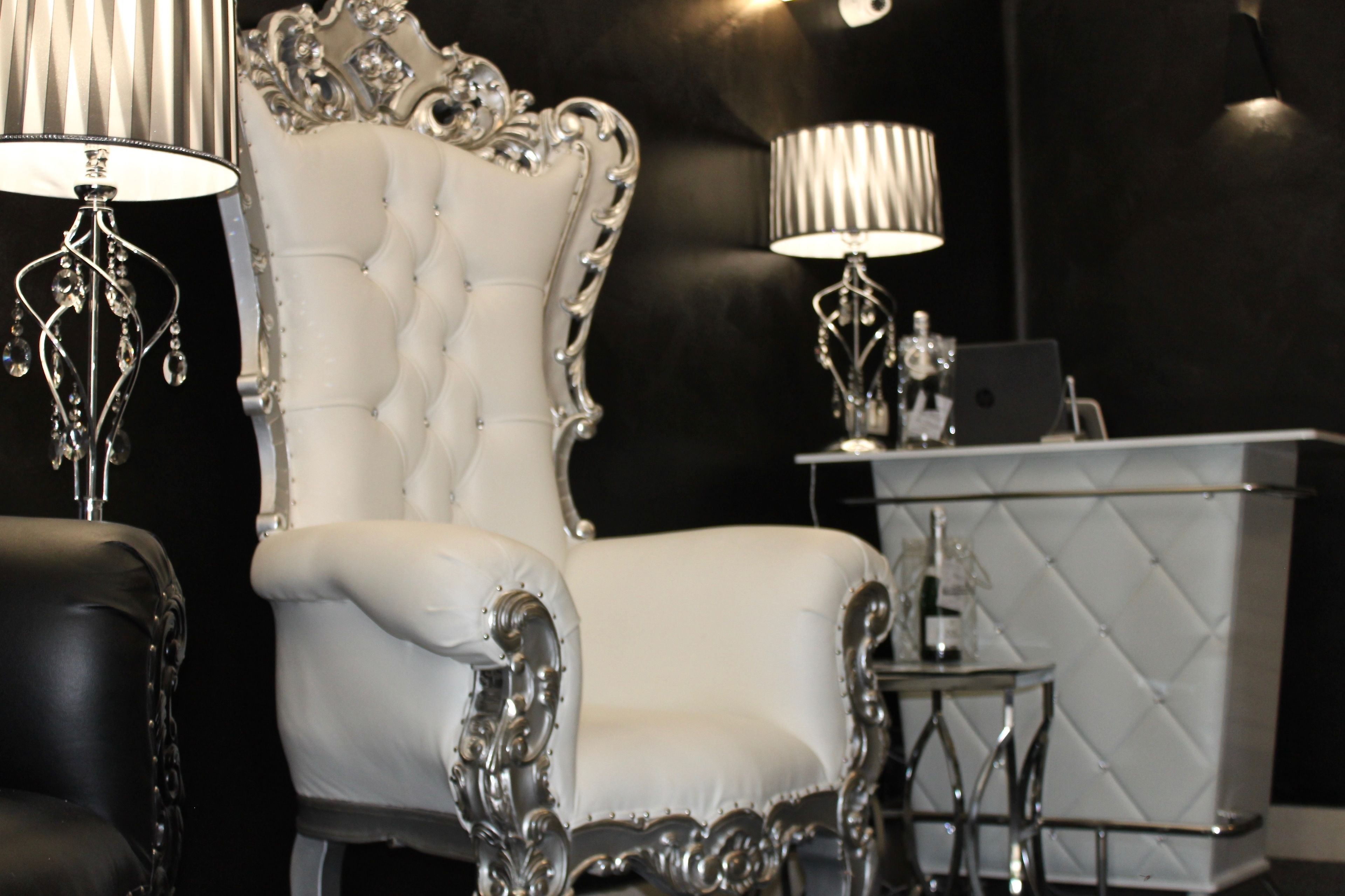 A luxurious room with a white tufted chair, a black leather sofa, and a modern reception desk.