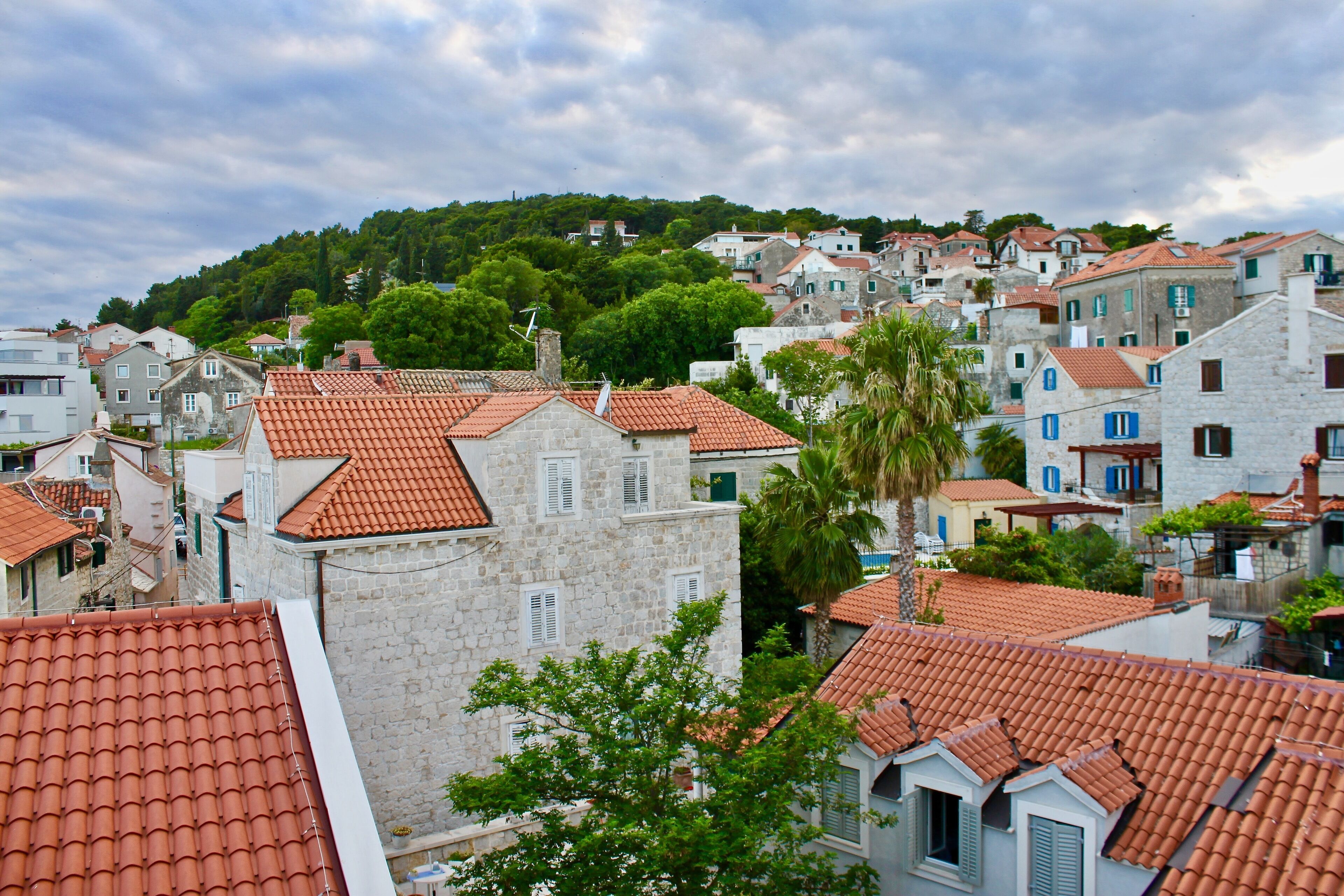 A coastal town with stone buildings and red-tiled roofs, surrounded by greenery and hills.