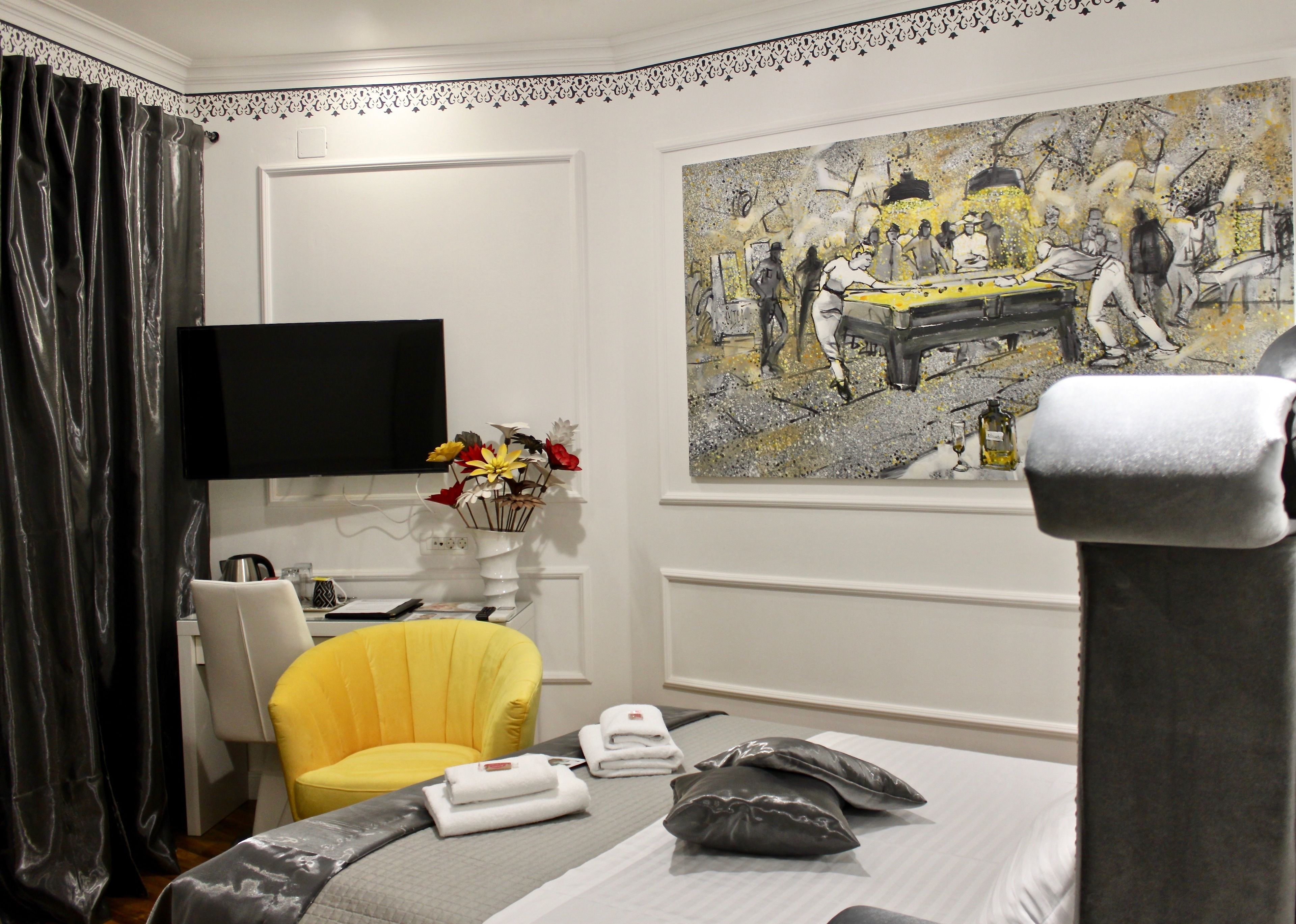 Ein Hotelzimmer mit Bett, Sessel, Gemälde, Fernseher und Blumen in einer Vase.