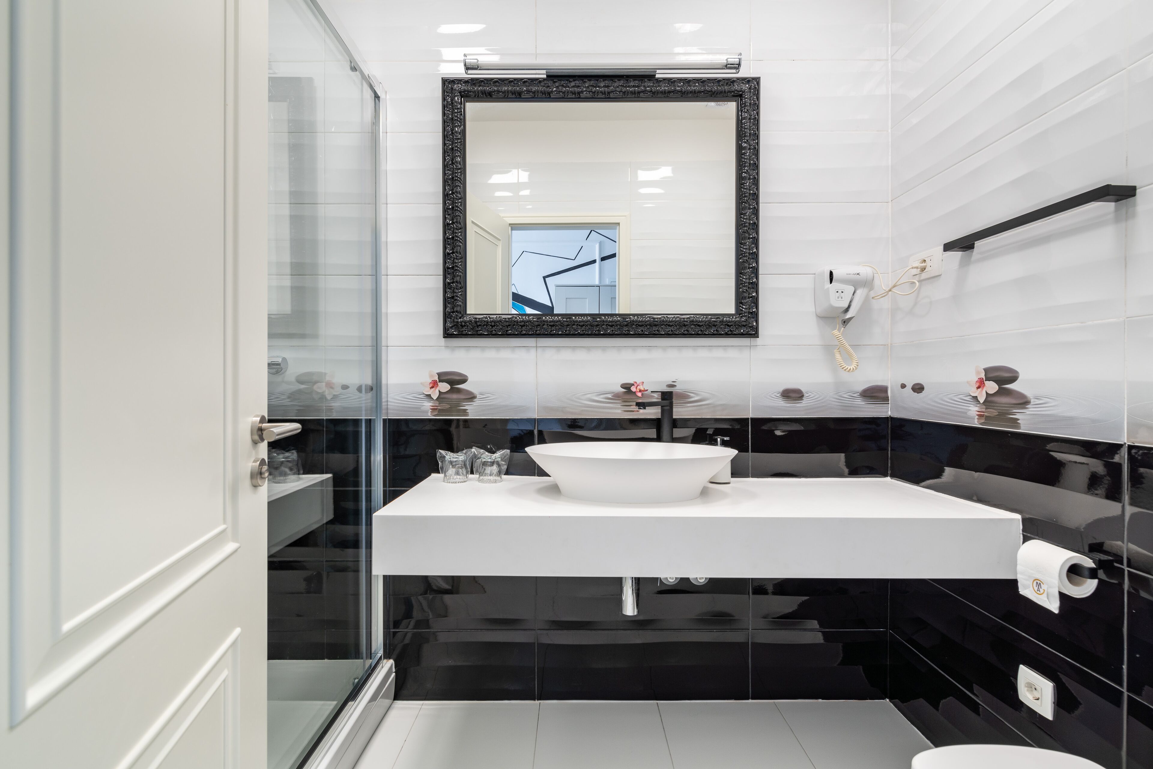 A modern bathroom with a white sink, black and white tiled walls, a large mirror, and a glass shower enclosure.