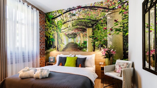 A bedroom with a large bed, a chair, a nightstand, and a wall mural of a garden. - Art & Garden Residence (Kraków)