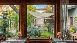 An outdoor dining area with tables set for two, surrounded by potted plants and a brick wall. - Art & Garden Residence (Kraków)