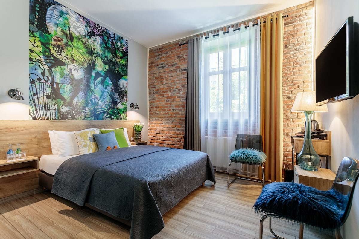 A modern hotel room with a large bed, a brick wall, a flat-screen TV, and a large abstract painting.