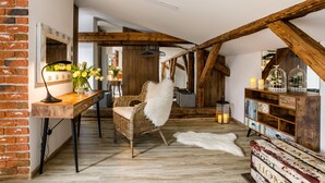 A rustic interior with exposed wooden beams, a brick wall, a wicker chair, a white fur throw, and a wooden cabinet with decorative items. - Art & Garden Residence (Kraków)
