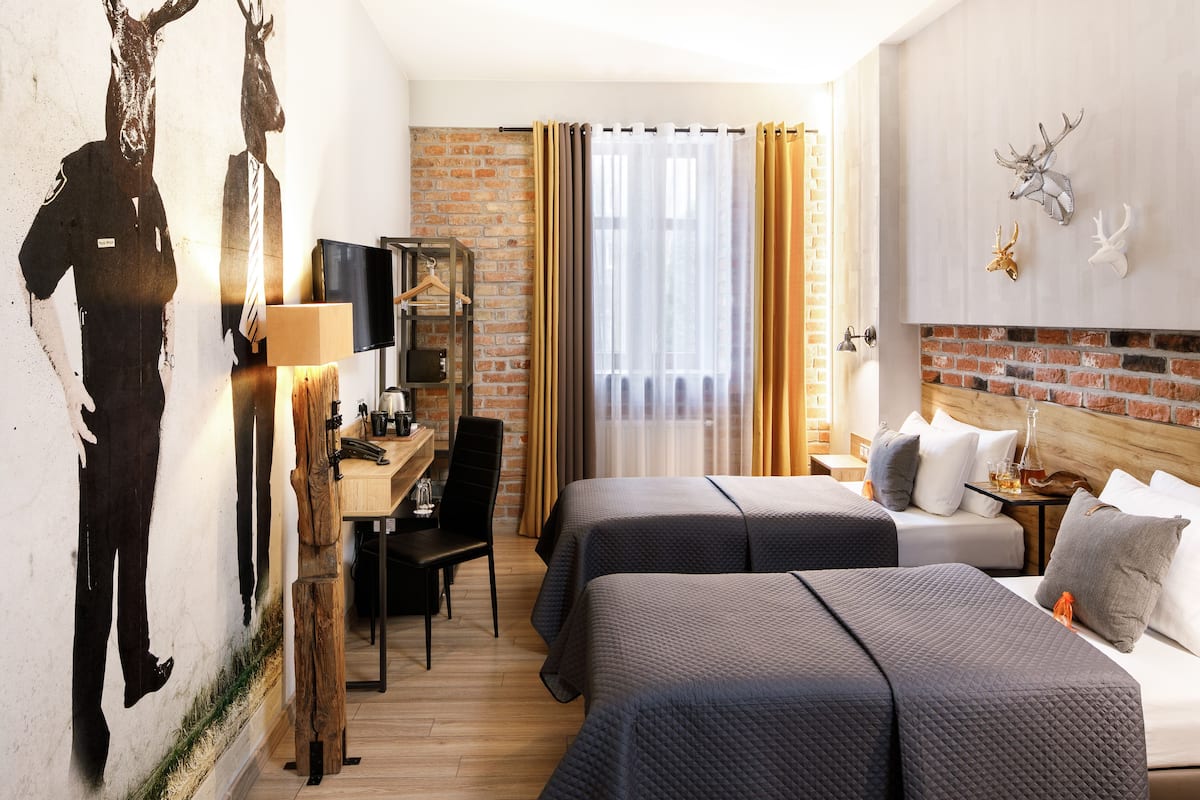 A hotel room with two beds, a desk, a TV, and a brick wall.