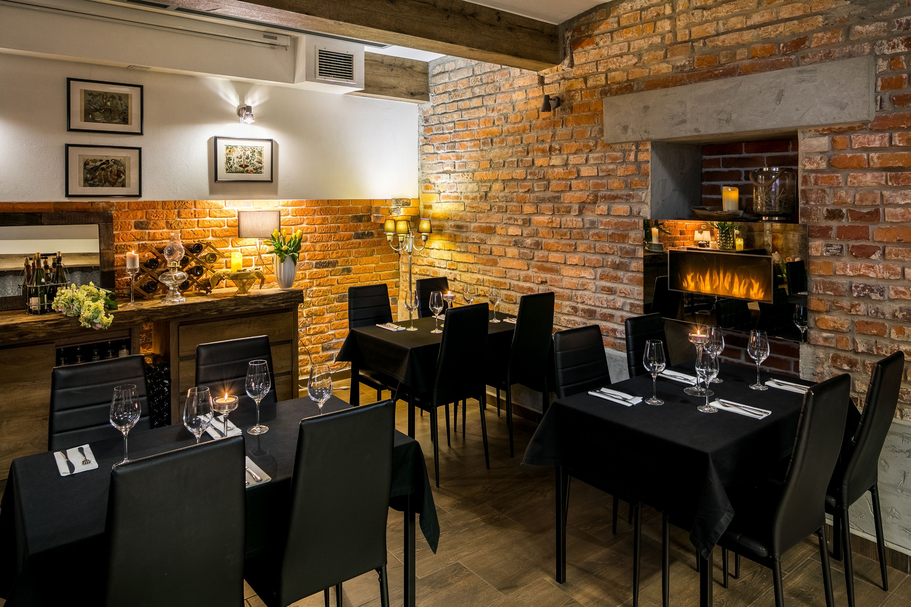 A restaurant with brick walls, black tables, and chairs. There are candles and a fireplace.