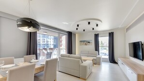 Una sala de estar moderna con comedor, un sofá, un televisor y un amplio ventanal con cortinas.
