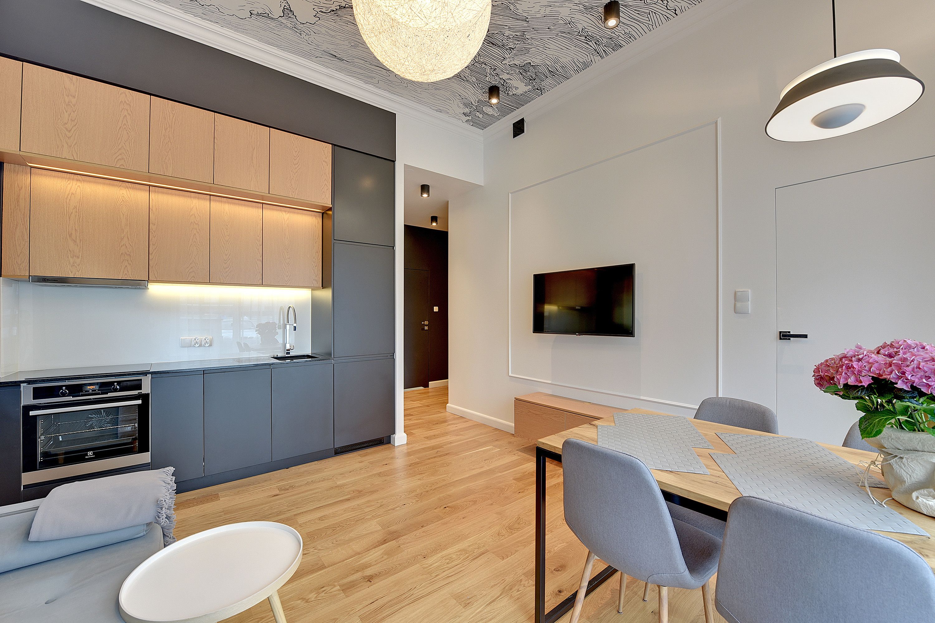 Een moderne keuken met houten kastjes, een inbouwoven en een eethoek met een tafel en stoelen.
