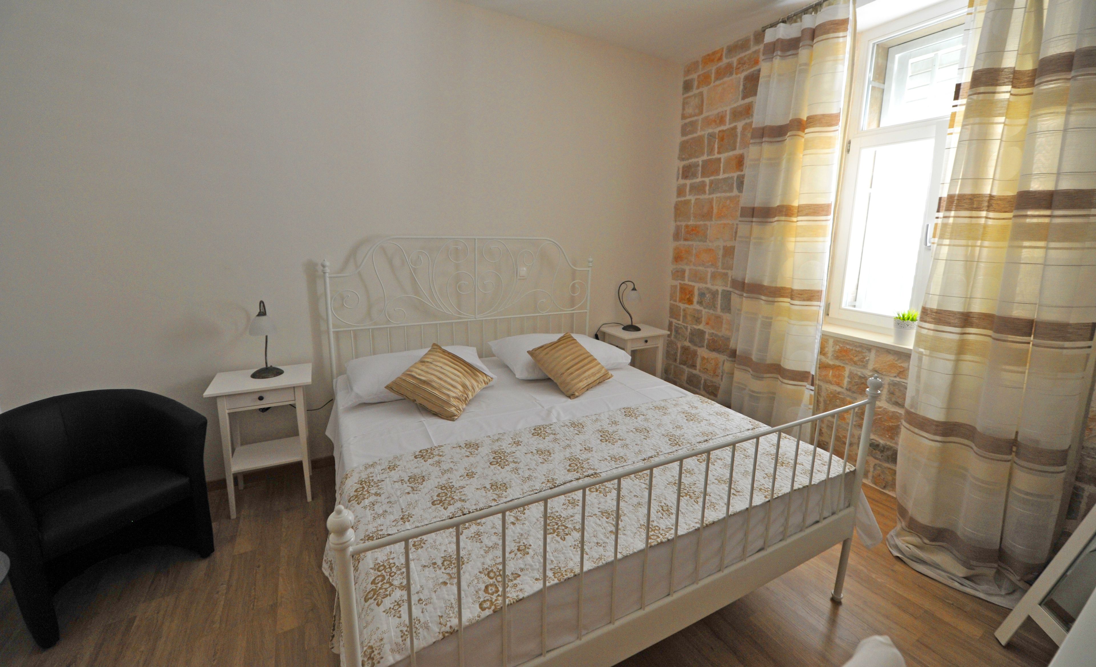 A bedroom with a single bed, a nightstand, a chair, and a window with curtains.