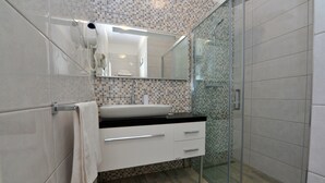 A bathroom with a glass shower enclosure, a white sink with a black countertop, and a tiled backsplash. - Nirvana Luxury Rooms (Split)