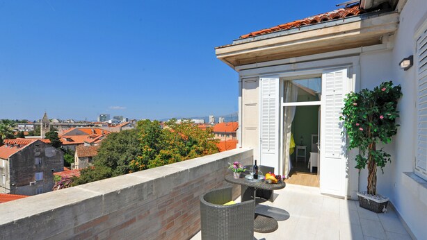 A balcony with a table set for dining, a potted plant, and a view of the cityscape. - Nirvana Luxury Rooms (Split)