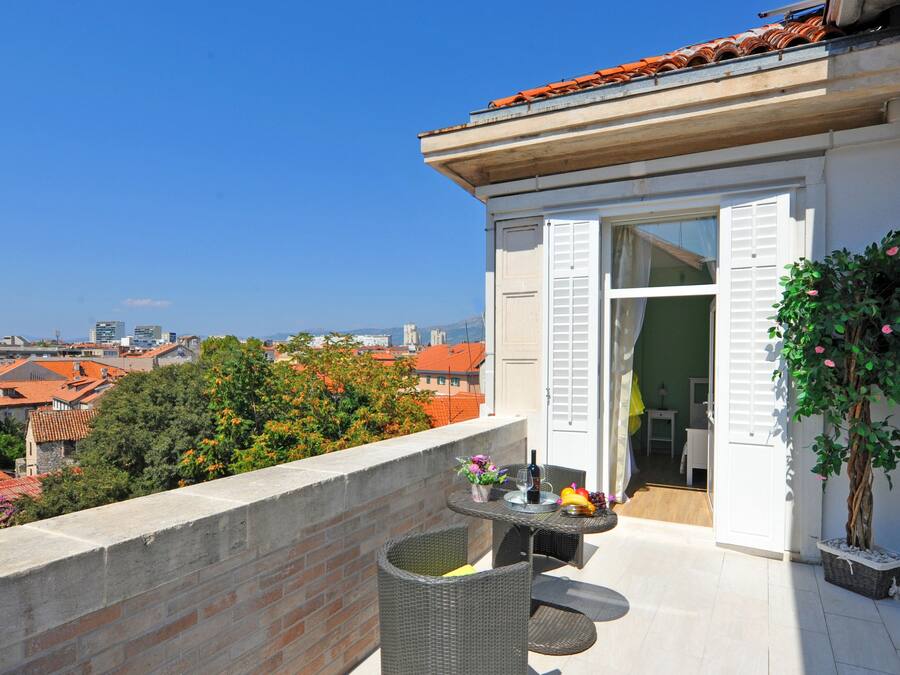 A balcony with a table set for dining, a potted plant, and a view of the cityscape.