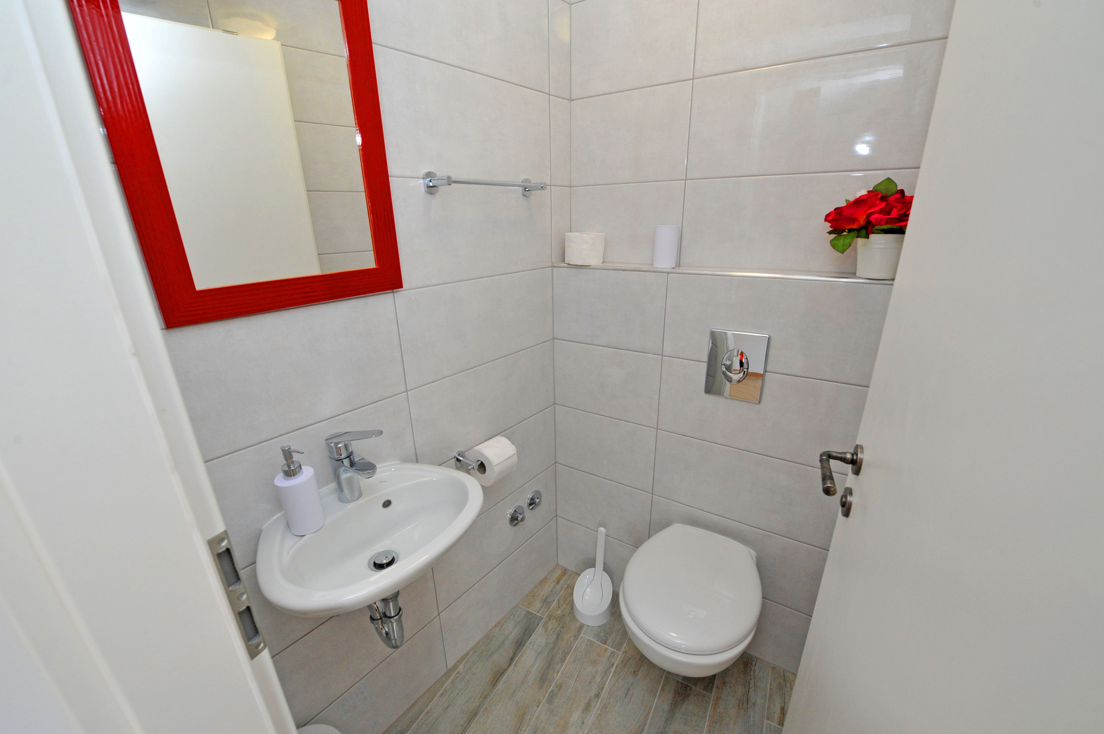 Un baño con lavamanos blanco, inodoro y espejo con marco rojo.
