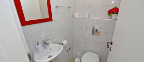 Un baño con lavamanos blanco, inodoro y espejo con marco rojo.