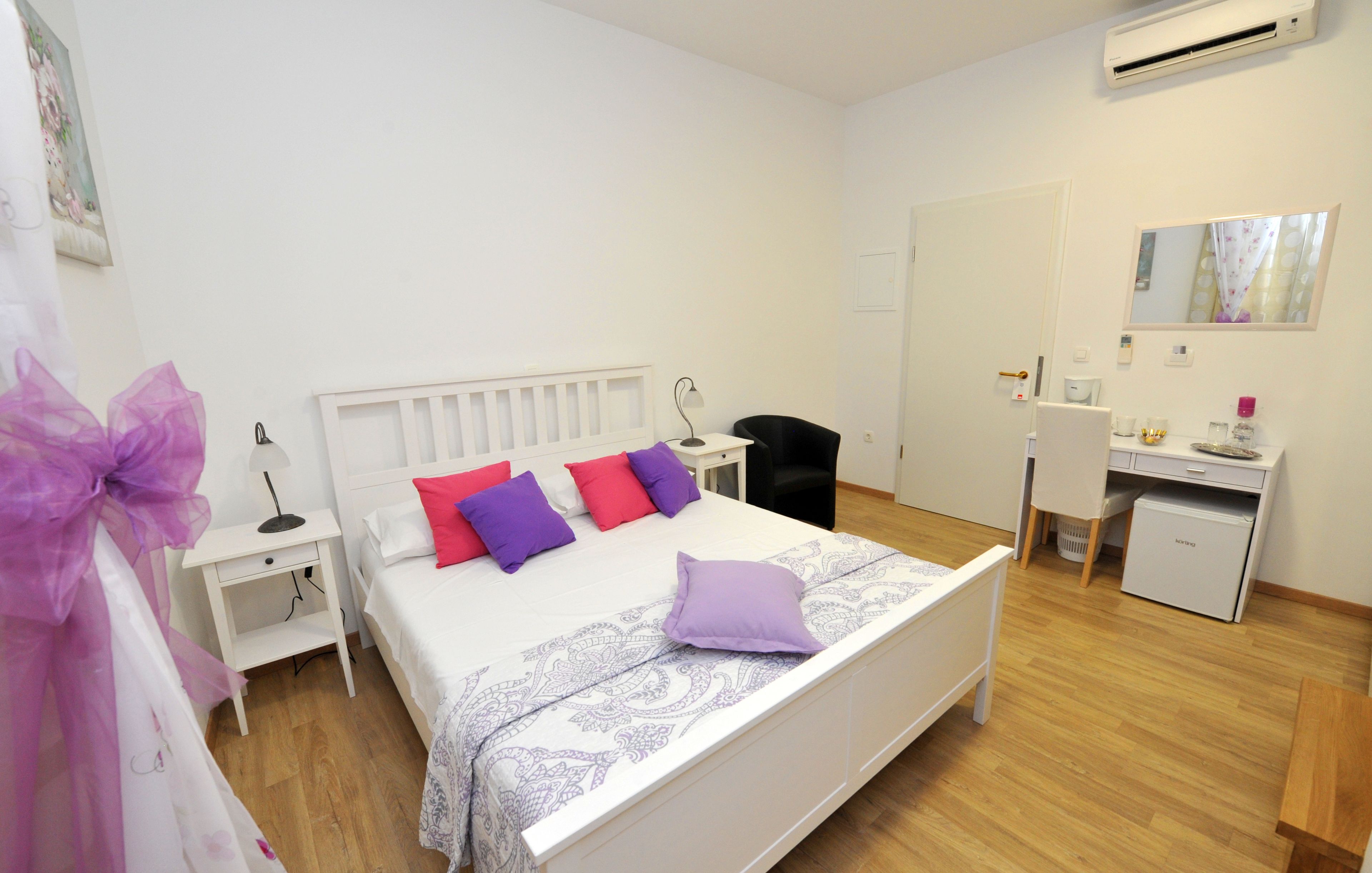 Un dormitorio con cama, mesitas de noche, escritorio, silla y aire acondicionado.