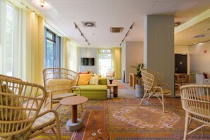 A hotel lobby with wicker furniture, a green sofa, a flat-screen TV, and a patterned carpet. - ibis Leipzig City (Leipzig)