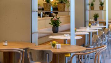 Interior de un restaurante con mesas redondas, sillas y estantes con plantas en macetas.