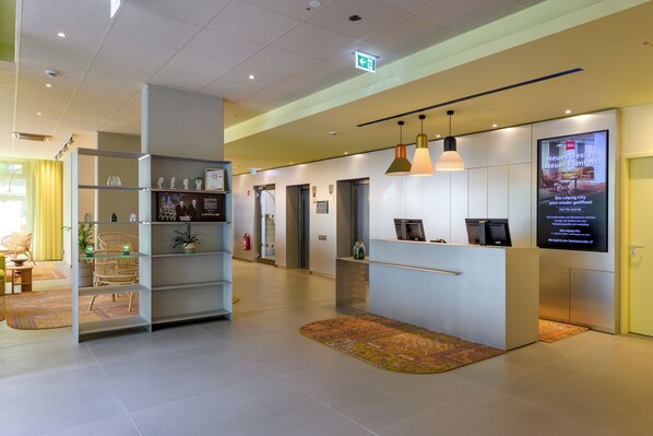 A reception area with a desk, chairs, a display board, and a fire extinguisher. - ibis Leipzig City (Leipzig)