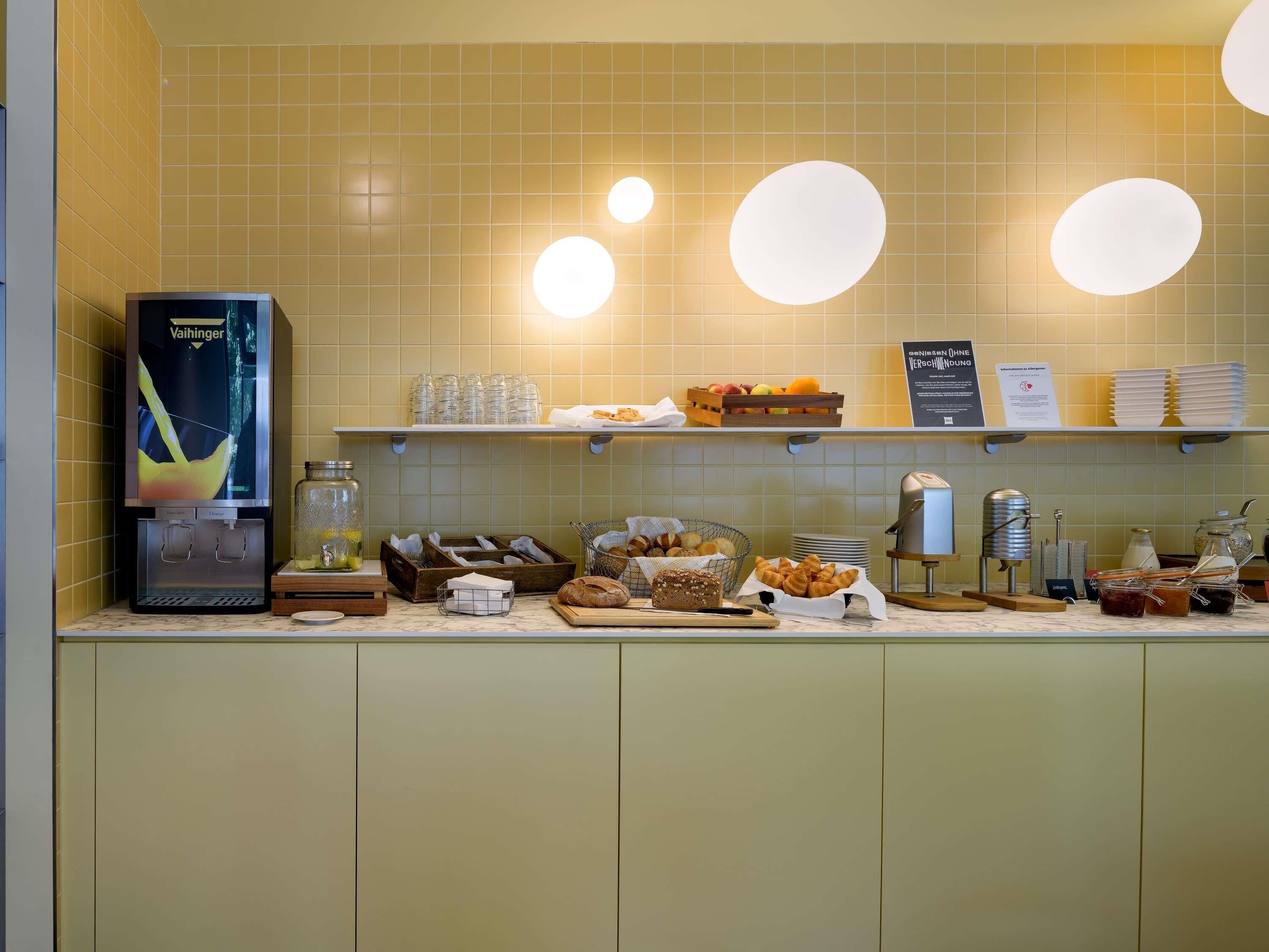Una barra de desayuno con refrigerador, repisas con platos y frutas, y una máquina de café.
