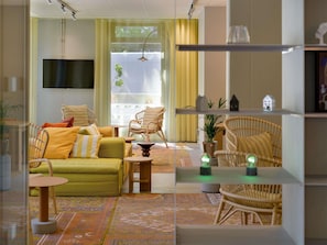 Un salon moderne avec un canapé, des fauteuils, un téléviseur et une grande fenêtre agrémentée de rideaux.