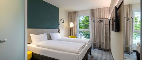 A hotel room with a bed, a TV, a window with curtains, a small table, and a chair.
