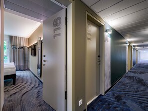 Et hotel med sengetøj, knagerække, dør med logo og et mønstret tæppe.