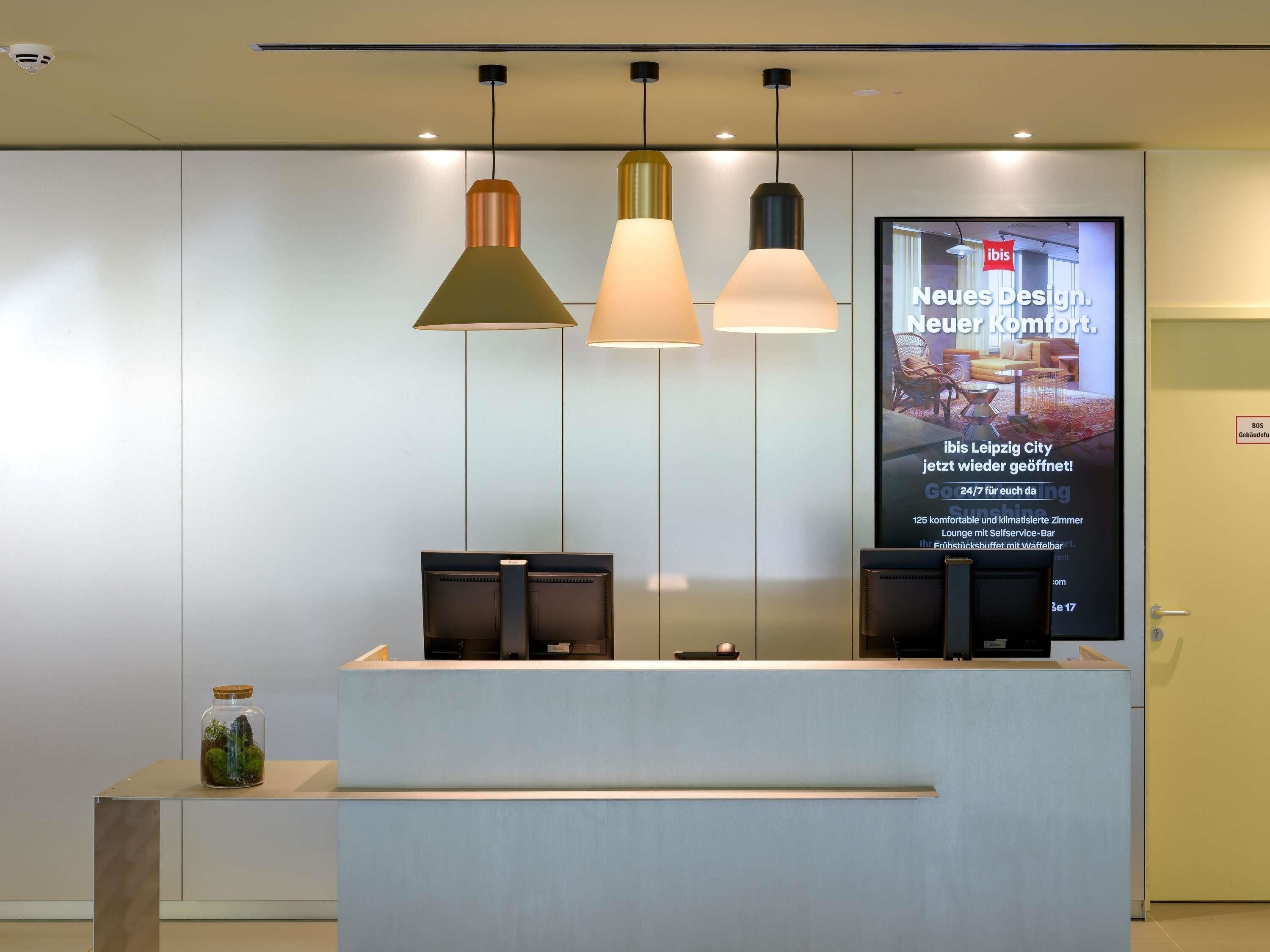 A reception desk with three pendant lights, a digital display with text, and a small plant on the counter.